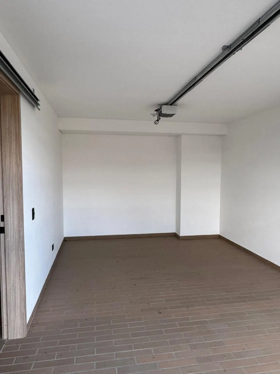 Parqueadero cubierto con piso en ladrillo y paredes blancas.