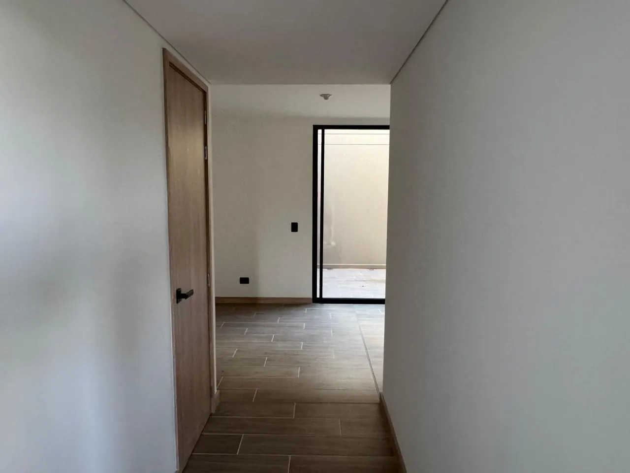 Pasillo de entrada con piso tipo madera que conduce al salón y al jardín interior.