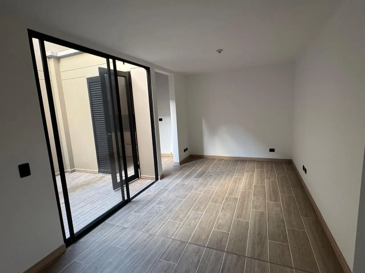 Salón-comedor con piso tipo madera y puerta corrediza de vidrio hacia el jardín interior.