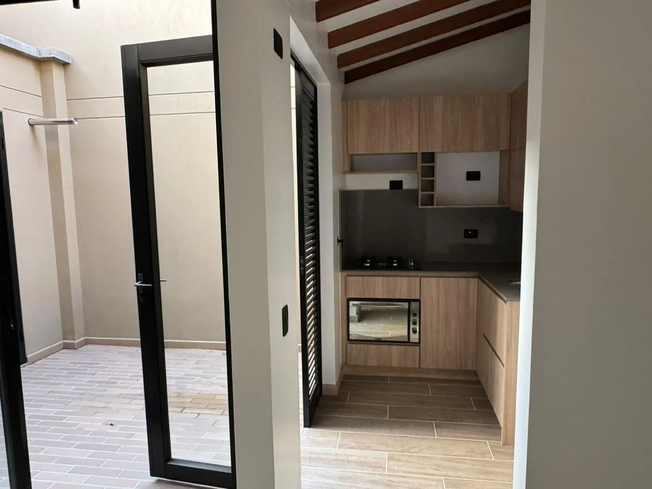 Cocina con techo de vigas de madera junto a la puerta de vidrio que da al jardín interior.