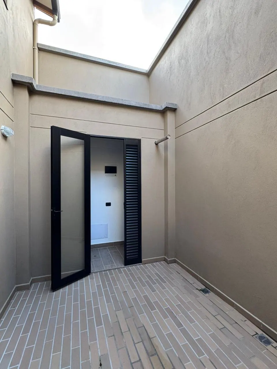 Jardín interior descubierto con piso en ladrillo y puerta hacia la zona de ropas.