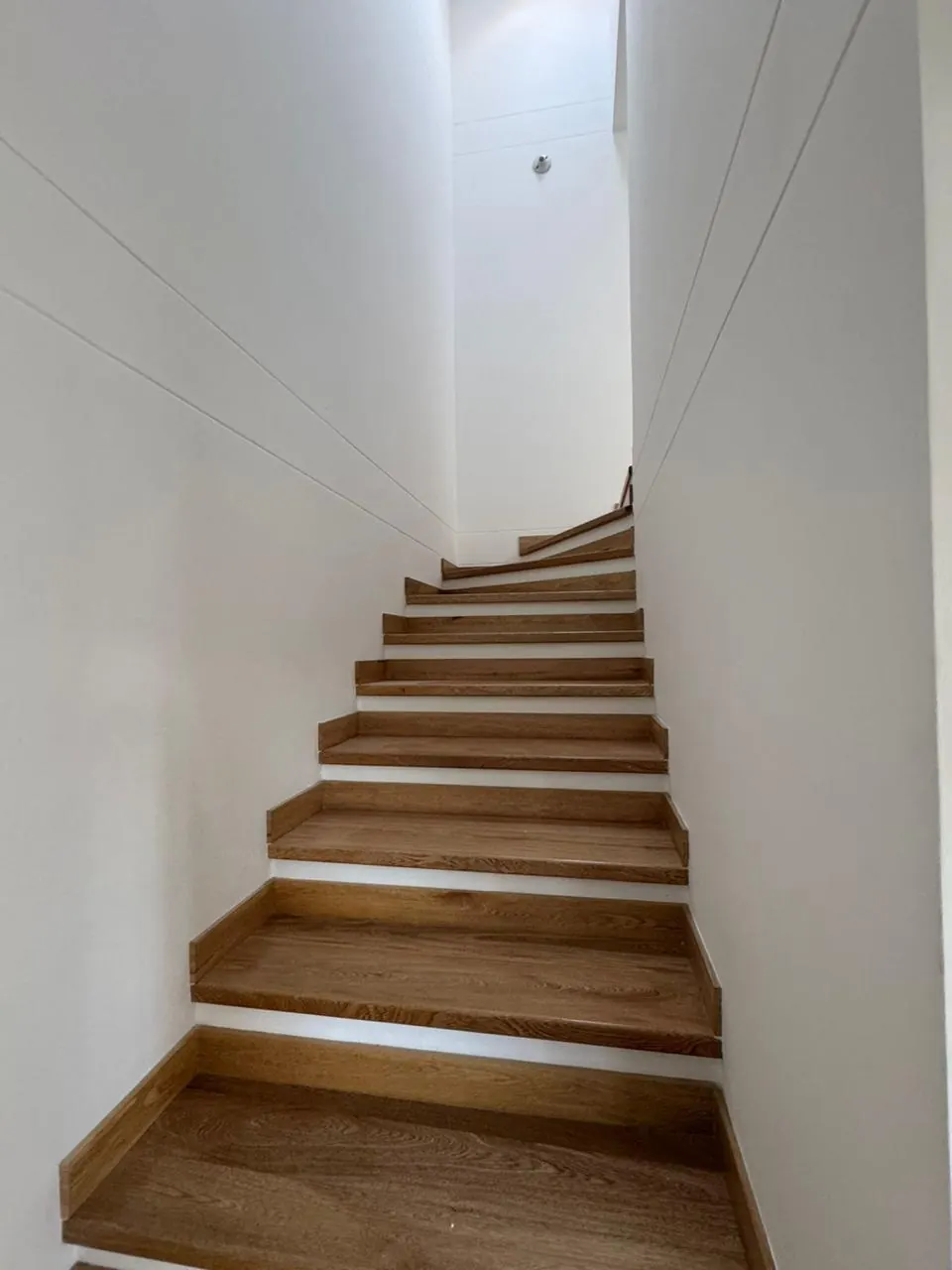 Escalera con peldaños en madera entre paredes blancas.