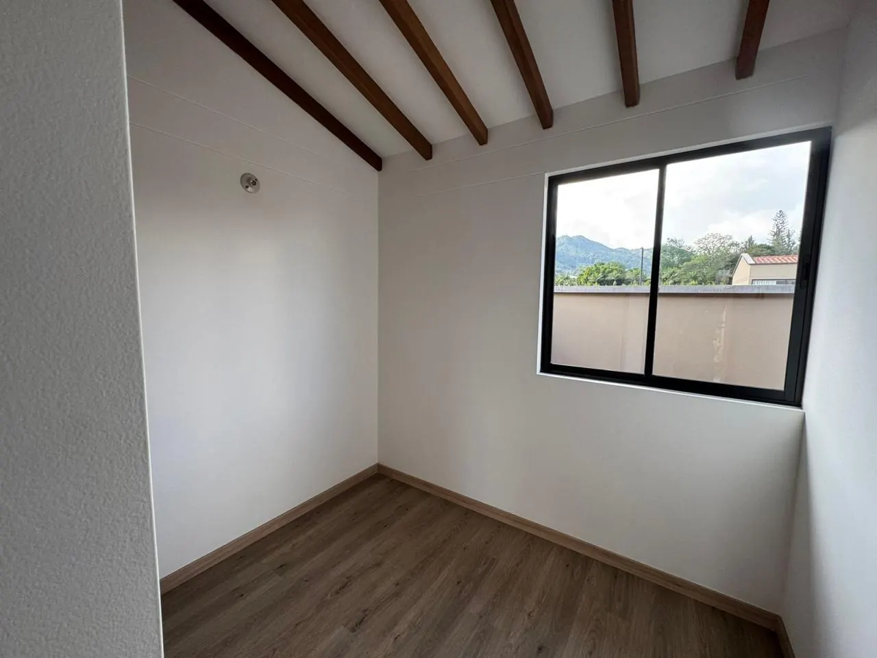 Alcoba con techo de vigas de madera y ventana con vista a las montañas.