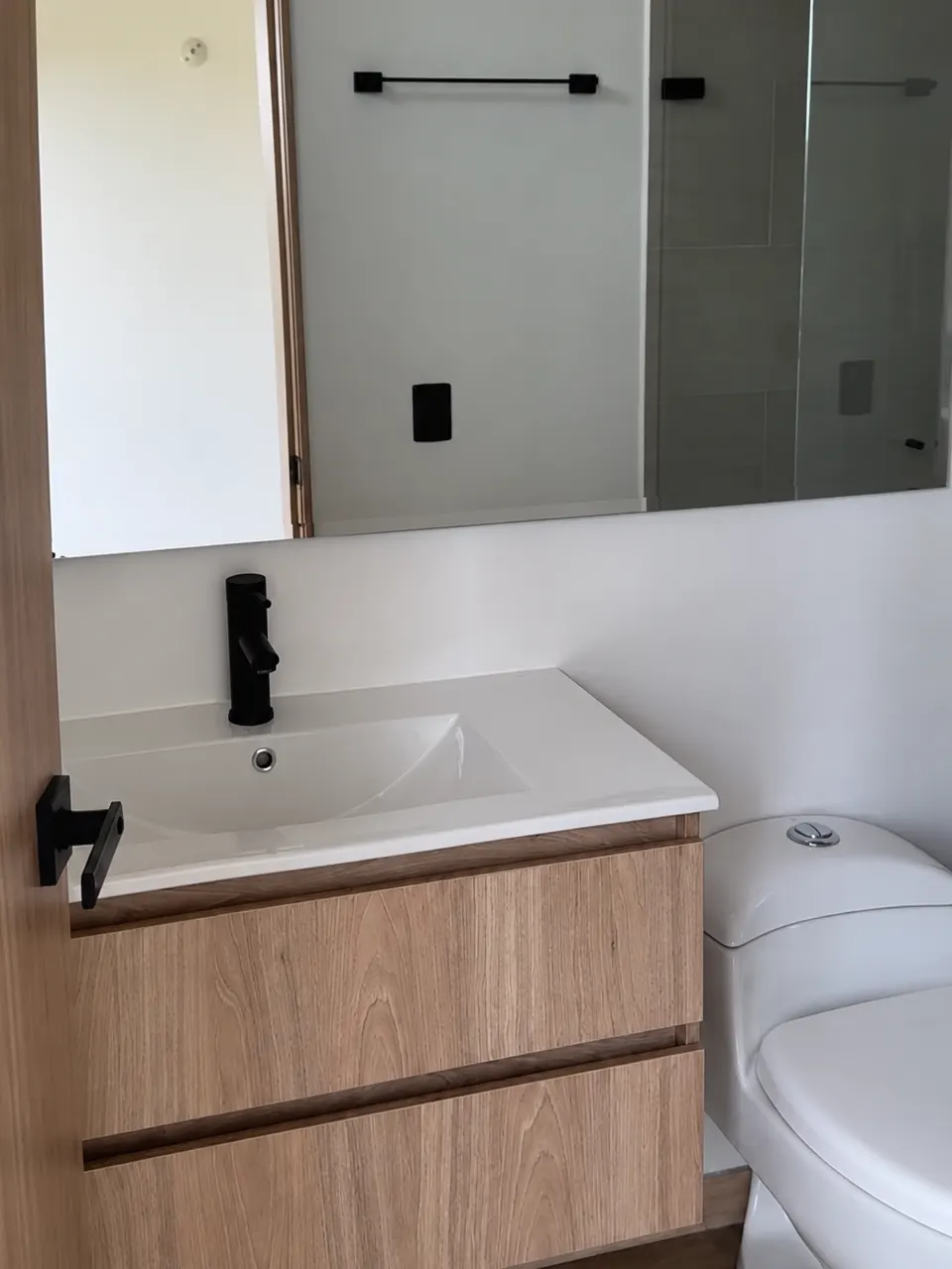 Lavamanos con mueble en madera clara, grifería negra y espejo amplio.