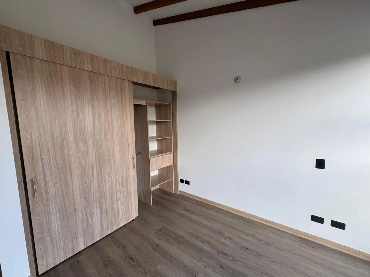 Alcoba con clóset de puerta corrediza en madera y piso tipo madera.